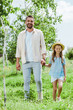 © LIGHTFIELD STUDIOS - happy father and daughter standing near green plants and holding hands