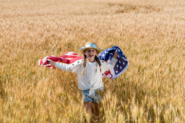 Poster - cheerful child holding american flag with stars and stripes in golden field