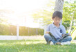 Asian little boy reading a book under tree.Child sitting on green grass at garden with sun light in morning day