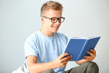 Male student reading book while preparing for exam on light background