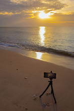 Close Up Of Smartphone Stuck To Tripod Taking Picture Of Sunset On Beach.