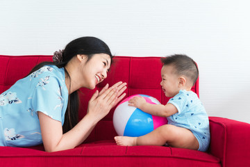 Mother play with her 8 month old son in blue dress on red sofa bed