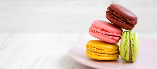 Sticker - Sweet and colorful macarons on a pink plate over white wooden background, side view. Copy space.