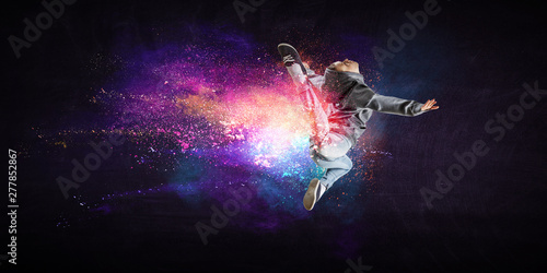 Modern female dancer jumping in hoodie with colourful splashes background. Mi...