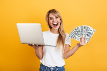 Poster - Positive optimistic emotional young blonde woman posing isolated over yellow wall background dressed in white casual t-shirt using laptop computer.