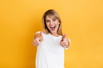 Wall Mural - Happy young pretty blonde woman posing isolated over yellow wall background dressed in white casual t-shirt.