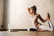© Drobot Dean - Photo of pretty concentrated woman doing yoga exercises using laptop while sitting on floor at home