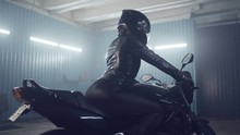 Stylish Brutal Biker Girl In A Black Glossy Helmet And Black Leather Jacket Is Sitting On His Bike. Neon Illumination. Preparation In The Night Races. Moto Service. Frame For The Film.
