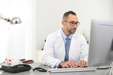 portrait of a handsome man male doctor in medical practice office working on computer