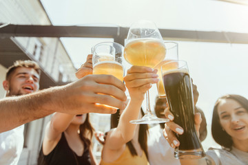 Young group of friends drinking beer, having fun, laughting and celebrating together. Women and men with beer's glasses in sunny day. Oktoberfest, friendship, togetherness, happiness, summer concept.