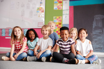 Portrait Of Elementary School Pupils Sitting On Floor In Classroom