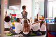 Elementary Pupils Wearing Uniform Raise Hands To Answer Question As Female Teacher Reads Book