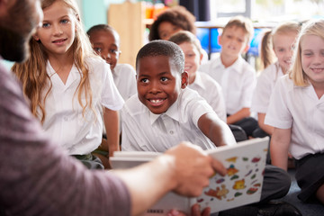 Wall Mural - Male Teacher Reading Story To Group Of Elementary Pupils Wearing Uniform In School Classroom