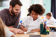 © Monkey Business - Male Elementary School Teacher Giving Female Pupil Wearing Uniform One To One Support In Classroom