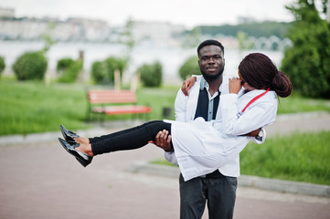 Wall Mural - Two young african american doctors couple in white coat. Man hold woman on hands.