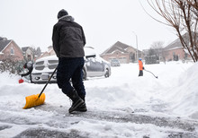 Man And Children Shovelling Snow Off Of A Driveway On A Snowy Day.