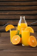 2 cups orange juice with slices of fresh orange, juice bottle on wooden background