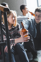 Wall Mural - smiling teenagers sitting on stairs, holding beer and talking