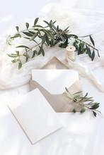Summer Wedding Stationery Mock-up Scene. Blank Greeting Cards, Envelope, Olive Branches And Silk Ribbon. White Background With Cotton Table Runner In Sunlight, Shadows. Flat Lay, Top View, Vertical