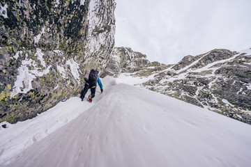 Wall Mural - An alpinist or a climber ascending steep snow alpine wall in harsh weather. Alpine mountauner climbing snow gully. Solo climber in winter High Tatras, Slovakia.