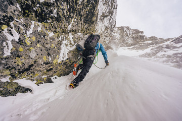 Wall Mural - An alpinist or a climber ascending steep snow alpine wall in harsh weather. Alpine mountauner climbing snow gully. Solo climber in winter High Tatras, Slovakia.