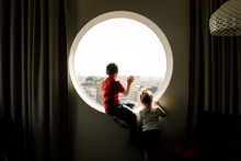 Rear View Of Siblings Looking Through Window