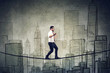 © pathdoc - Businessman walking balancing on a rope above a city