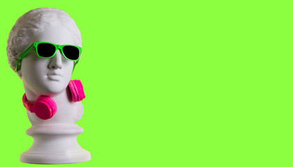 Wall Mural - Statue. Earphone. Isolated. Gypsum statue of Aphrodite's head. Creative. Plaster statue of Aphrodite's head in green sunglasses. On a green background.