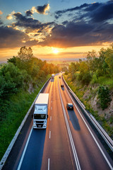 Wall Mural - three white truck and three private car driving on the asphalt road in a rural landscape at sunset w