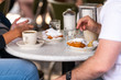 © Andriy Blokhin - Closeup of couple sitting outside at sidewalk cafe by table drinking chicory coffee and eating deep fried beignet donut powdered with sugar