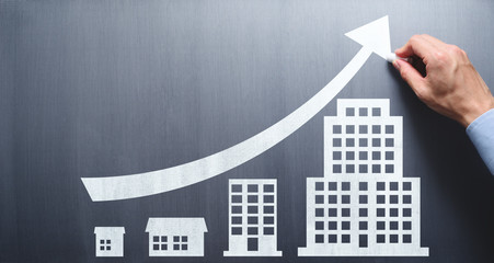 Wall Mural - Business development into large company. Business education. Businessman drawing office buildings and growth arrow on chalkboard.