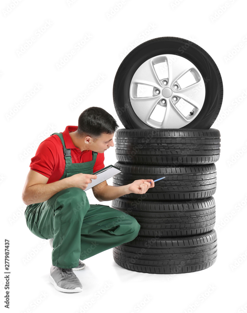 Young male mechanic in uniform with car tires on white background