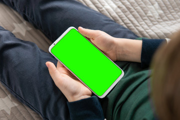 Wall Mural - Phone a for keying is holding kid. Smartphone with a hromakey in the hands of a child close up top view . Smartphone with a green screen in hand child .