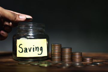 Hand holding coins dropping to the glass jar on old wood plank ,saving money concept.