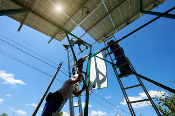 Two mounters installing solar batteries on metallic carcass. Innovative solution for natural resources saving, using renewable solar energy. Environment friendly, green energy. Modern equipment.