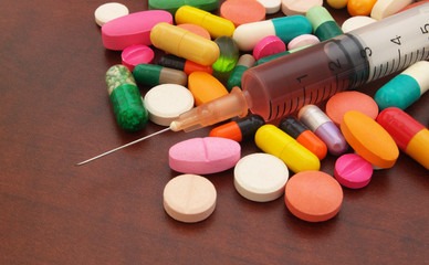 Colorful drugs, pills and syringe on wooden table close up, pharmacy and medical concept.