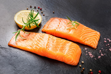 Raw salmon with spices on a black background. Two slices of fresh fish with lemon, rosemary, salt, and pepper