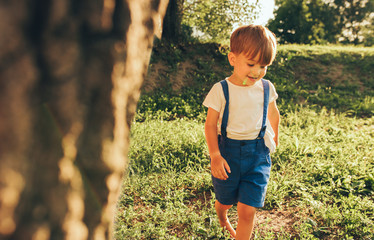 Image of happy little boy wearing blue shorts smiling and playing at sunlight and nature background. Adorable child running on the green grass in the park. Kid having fun. Childhood