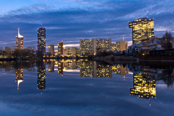 Modern cityscape with skyline of office skyscrapers in Vienna and reflections seen from Danube oxbow lake at dusk.