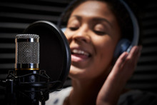 Female Vocalist Wearing Headphones Singing Into Microphone In Recording Studio