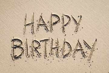 Wall Mural - Happy Birthday message handwritten in all capital letters in smooth beach sand under bright sunlight