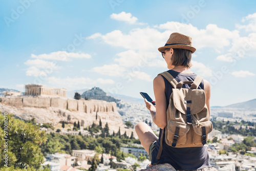 Young woman using smart phone in Athens with Acropolis at the background. Traveler girl enjoying vacation in Greece. Summer holidays, vacations, travel, tourism, technology concept.