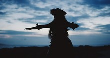 Silhouette Of A Traditional Hawaiian Hula Dancer Woman Dancing On A Rugged Island Landscape At Dusk In Slow Motion With An Ocean Background