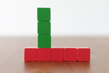 Stacked green wooden blocks on top of red wooden cubes on wooden table 