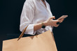 © LUMINA IMAGES - Unrecognisable cropped woman holding shopping bags and typing on her smartphone.