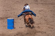 Barrel Racing at a Rodeo, a cowgirl rides a roan colored horse has rounded a barrel and is headed to the finish. Her legs are out in the stirrups. The dirt is flying as the horse digs in for speed.