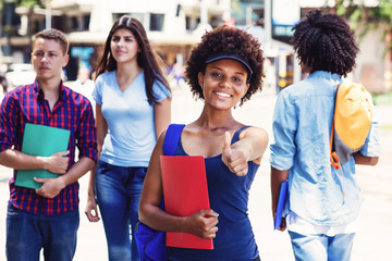 Wall Mural - Laughing african american young adult woman with students in city