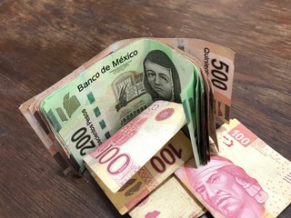 Many mixed mexican peso bills spread over a wooden desk