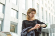 © bodnarphoto - Attractive young woman in a rush looking at the watch on her wrist checking time. Cute girl waiting for a partner to go on the meeting near the office building.