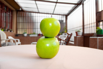 Two green apples on top of each other placed on the table in the garden.